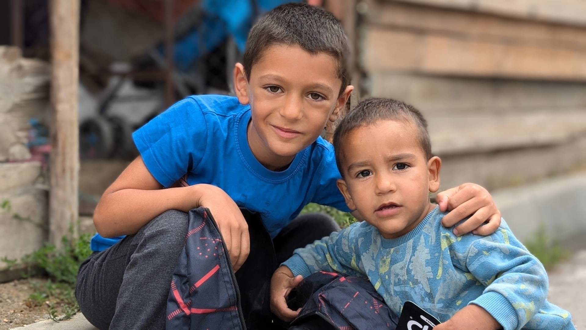 Smiling dark-haired boy with new backpack kneels beside his younger brother.