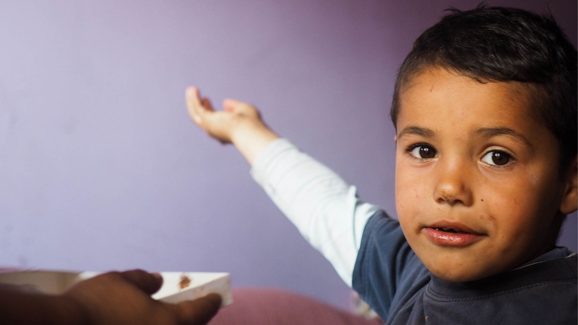 Boy with black hair reaches out one arm as if catching something in air.