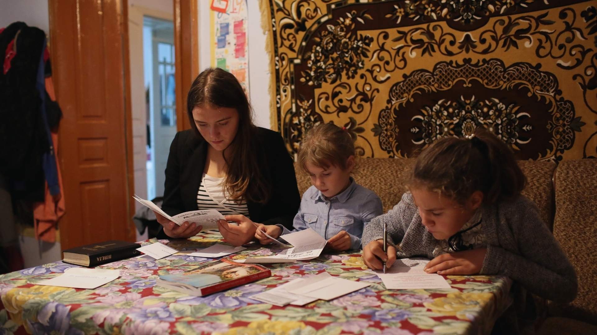 Young woman and two girls sitting at desk doing assignments