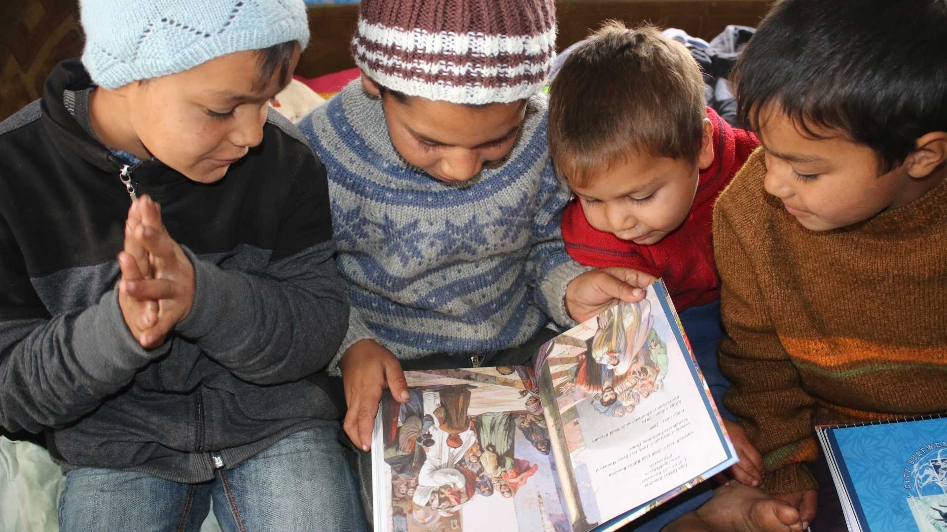 Four young boys sitting together on a bed, reading from a brightly illustrated children’s Bible.