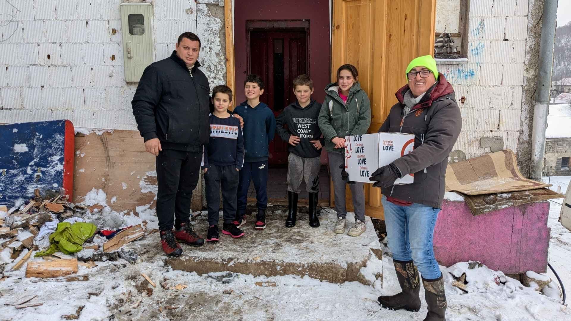 A man delivering a box to a family outside their home in the snow.
