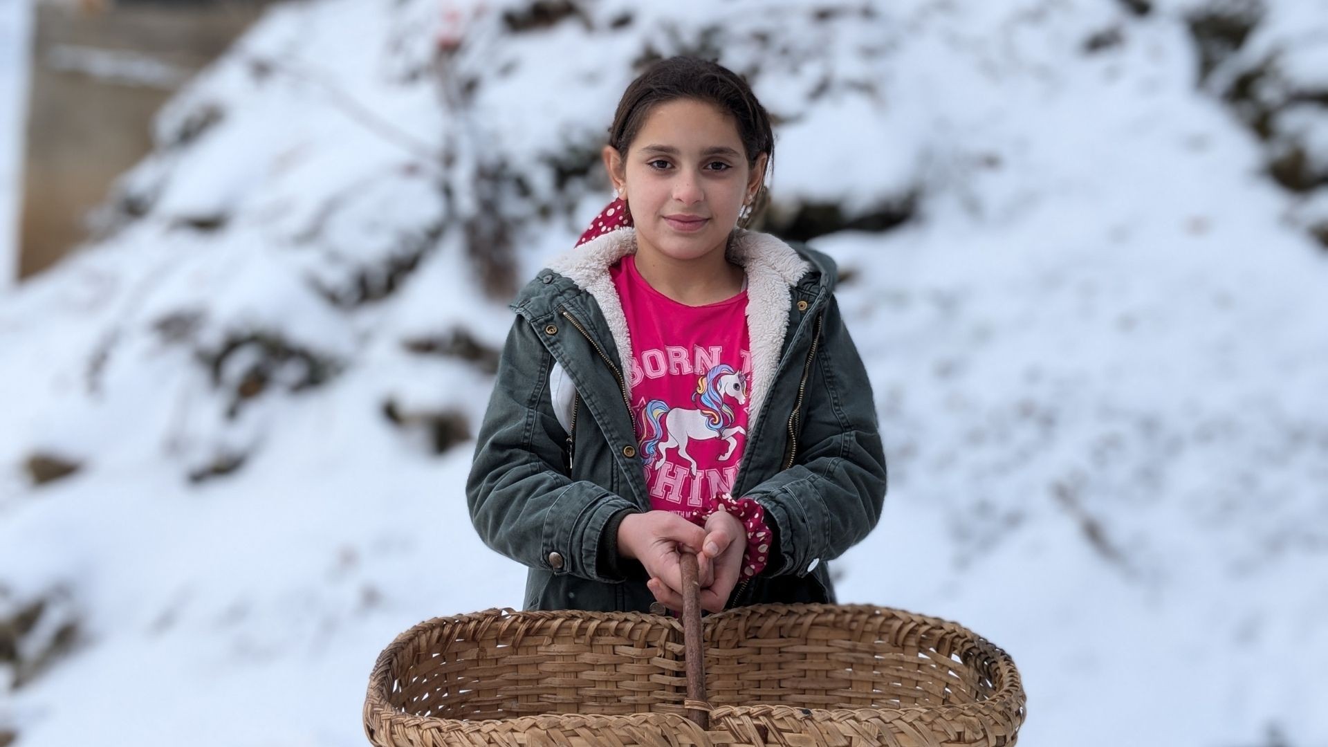 Young girl standing outside in the snow holding an empty basket.