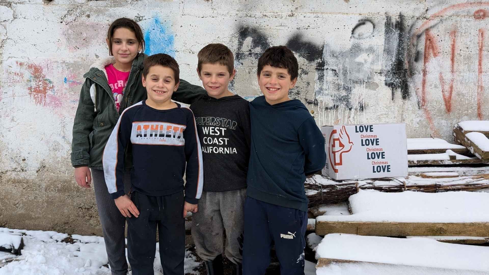 Four children standing in the snow beside a Christmas box.