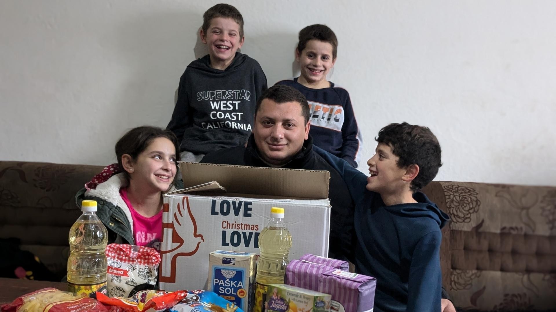 Smiling family gathered around an unpacked box of food.