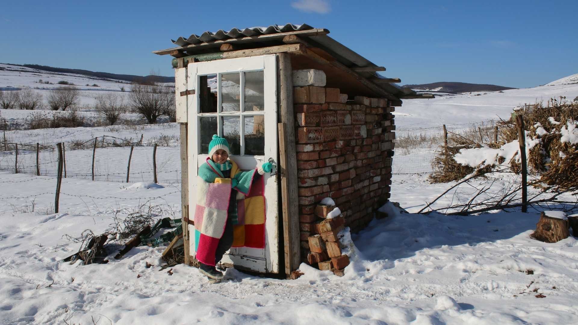 A young boy wrapped in a knitted blanket outside in the snow