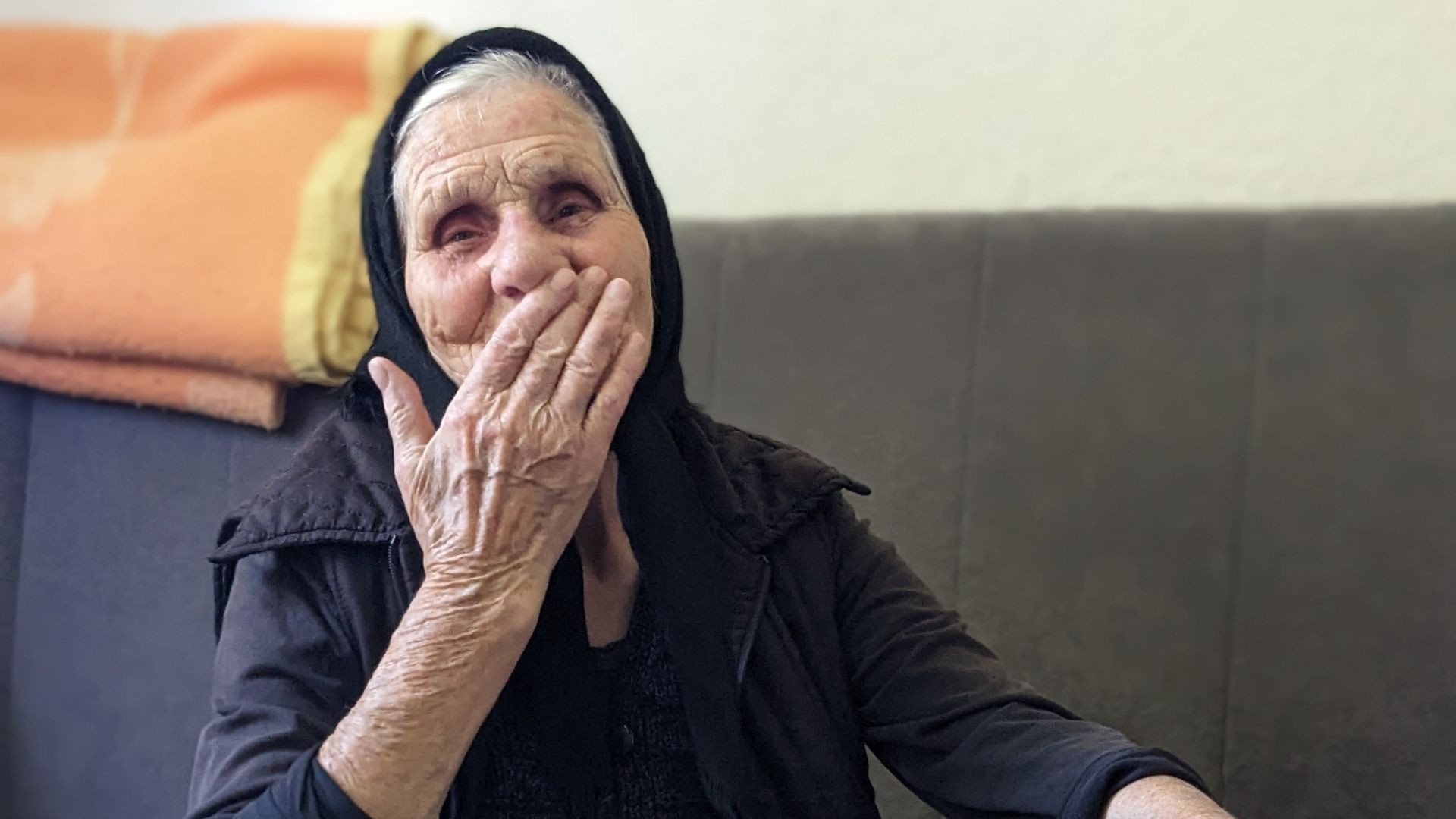 Elderly woman with her hand in front of her mouth, smiling