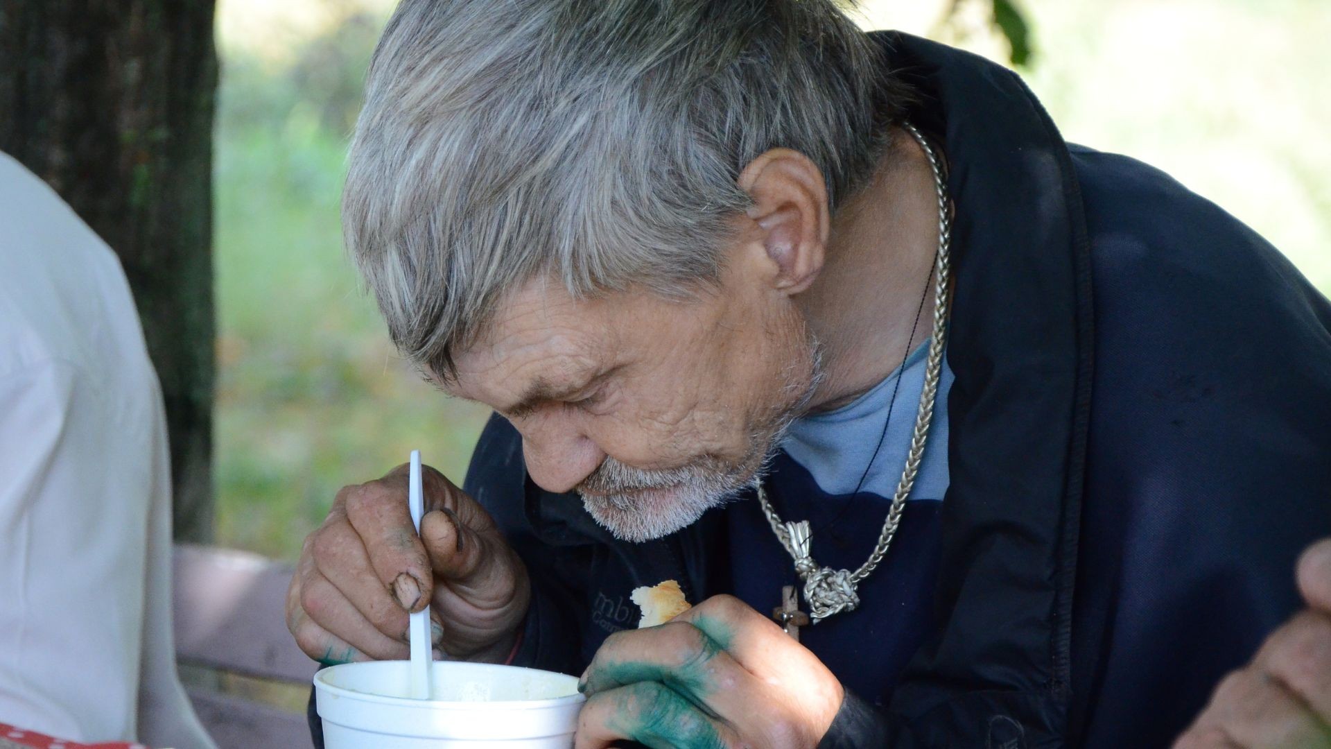Homeless man seated among others, quietly eating a warm meal with his head bowed.