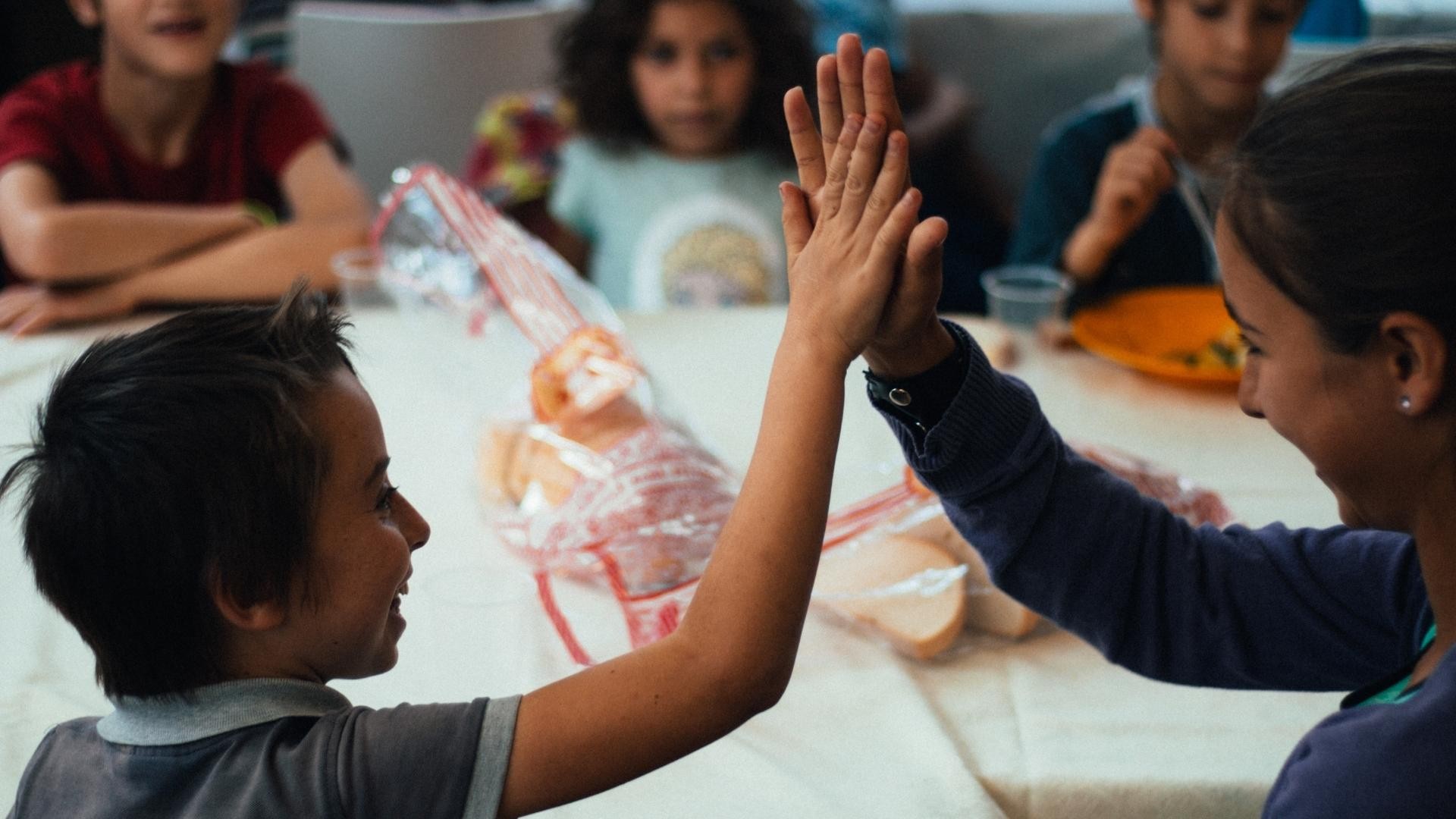 Smiling child shares a high-five with his tutor at an after-school club dining table.