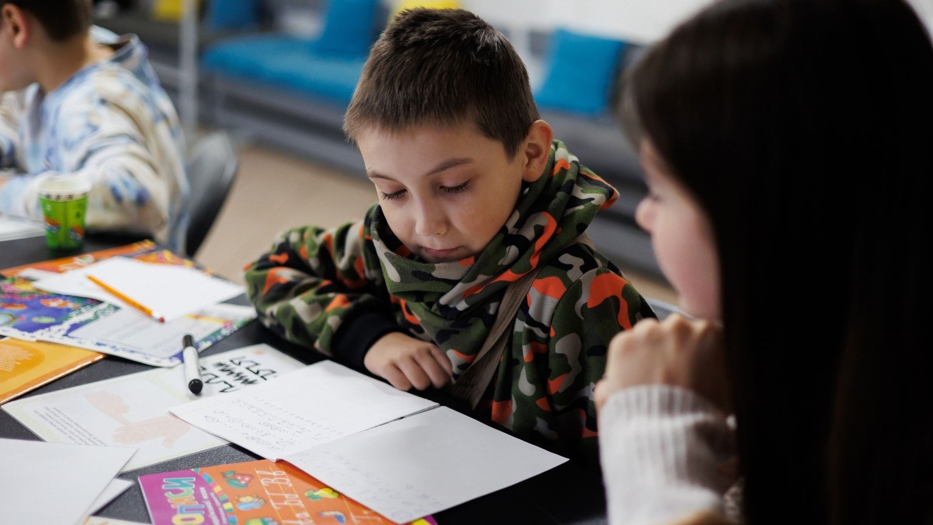 Boy sitting at a desk, receiving guidance from a tutor while completing his homework.