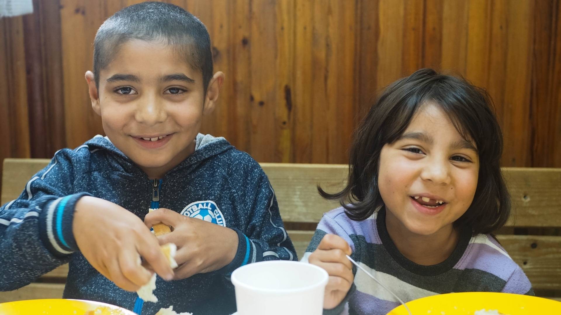 Two children smile as they enjoy a meal together at an after-school programme.