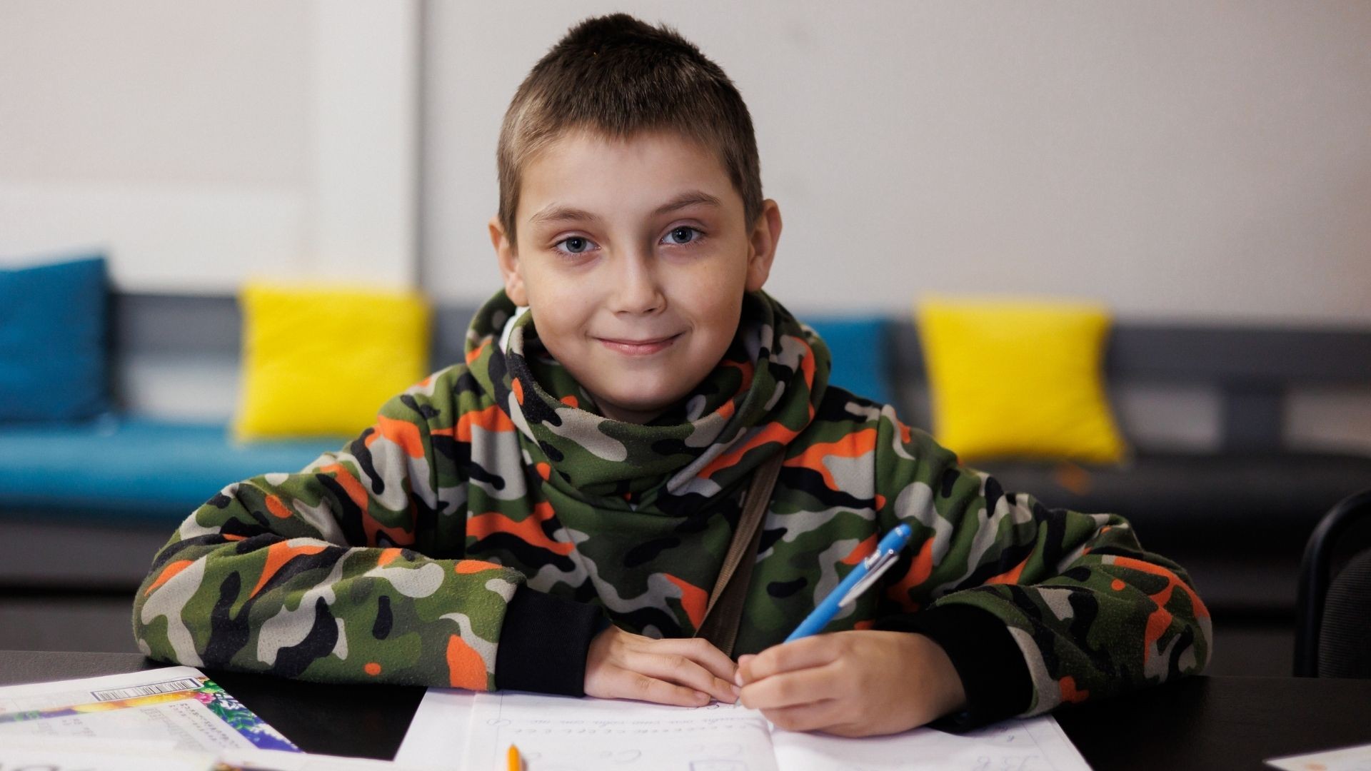 A young boy in a camouflage sweater writes in his exercise book.