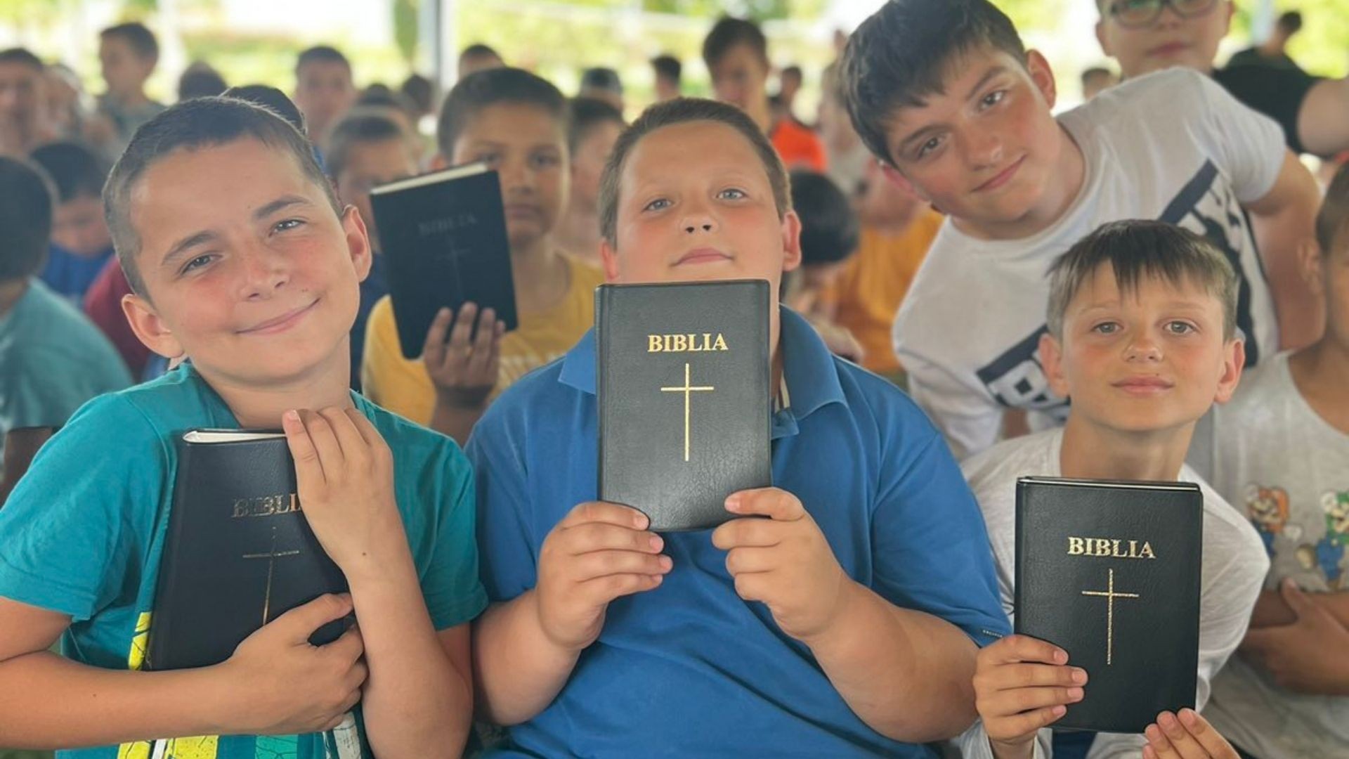Boys at camp smile proudly, holding their new Bibles.
