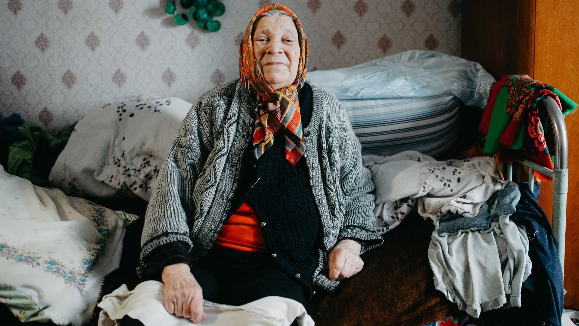 Elderly Nina from Ukraine sits on her bed