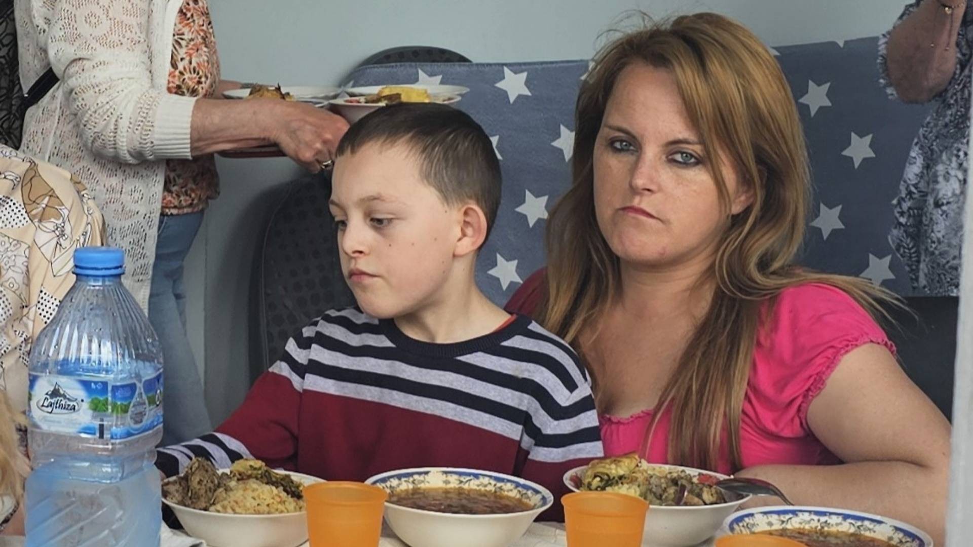 Child sits on mother’s lap as a warm meal is served at the table.