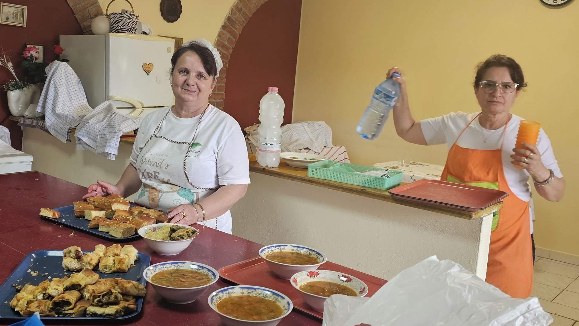 Two soup kitchen staff prepare food together, readying meals for guests. 