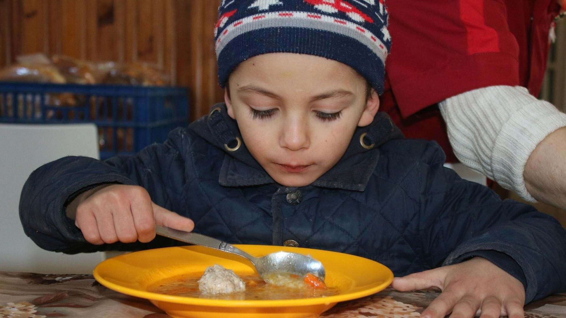 Young boy in knitted hat enjoys a warm bowl of soup at the table.