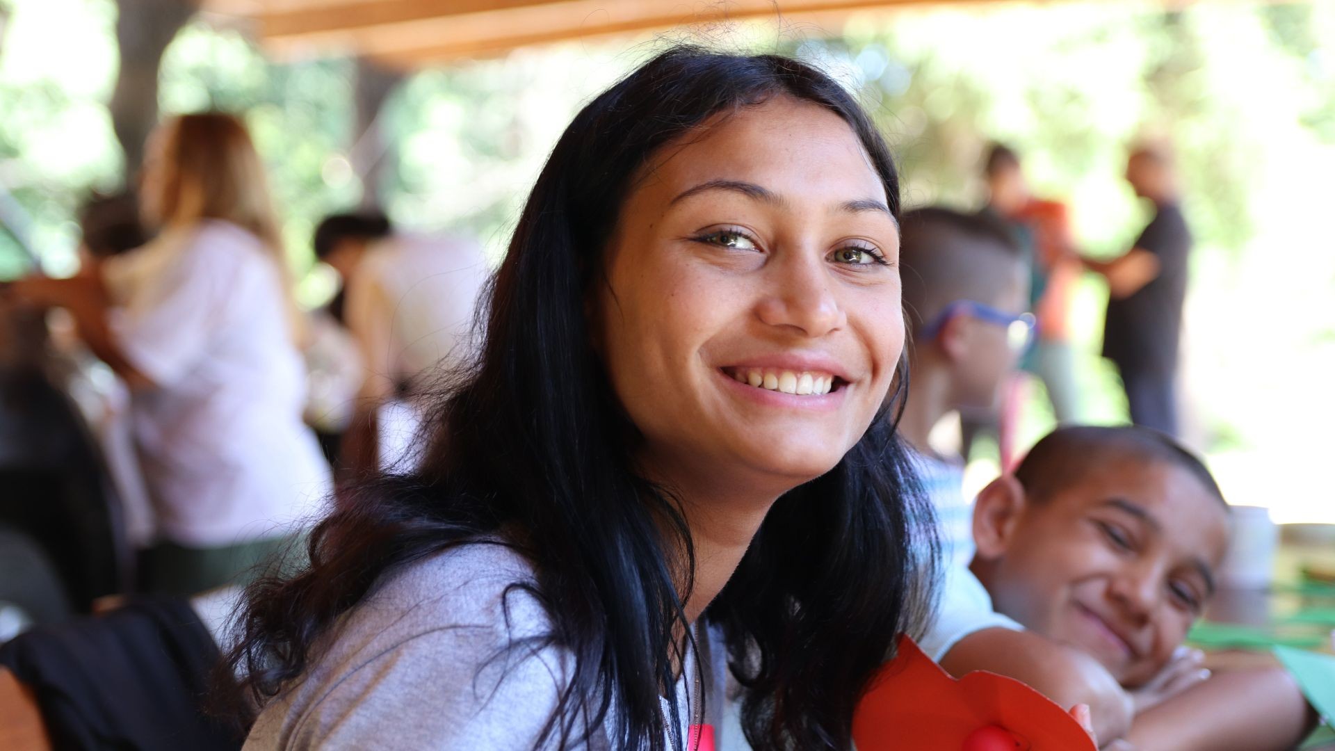 Smiling young girl looking at the camera, with other children in the background at a summer camp.