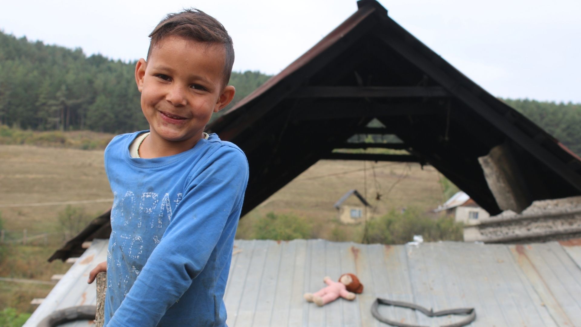 Smiling young boy standing elevated with an A-frame roof and expansive landscape in the background.
