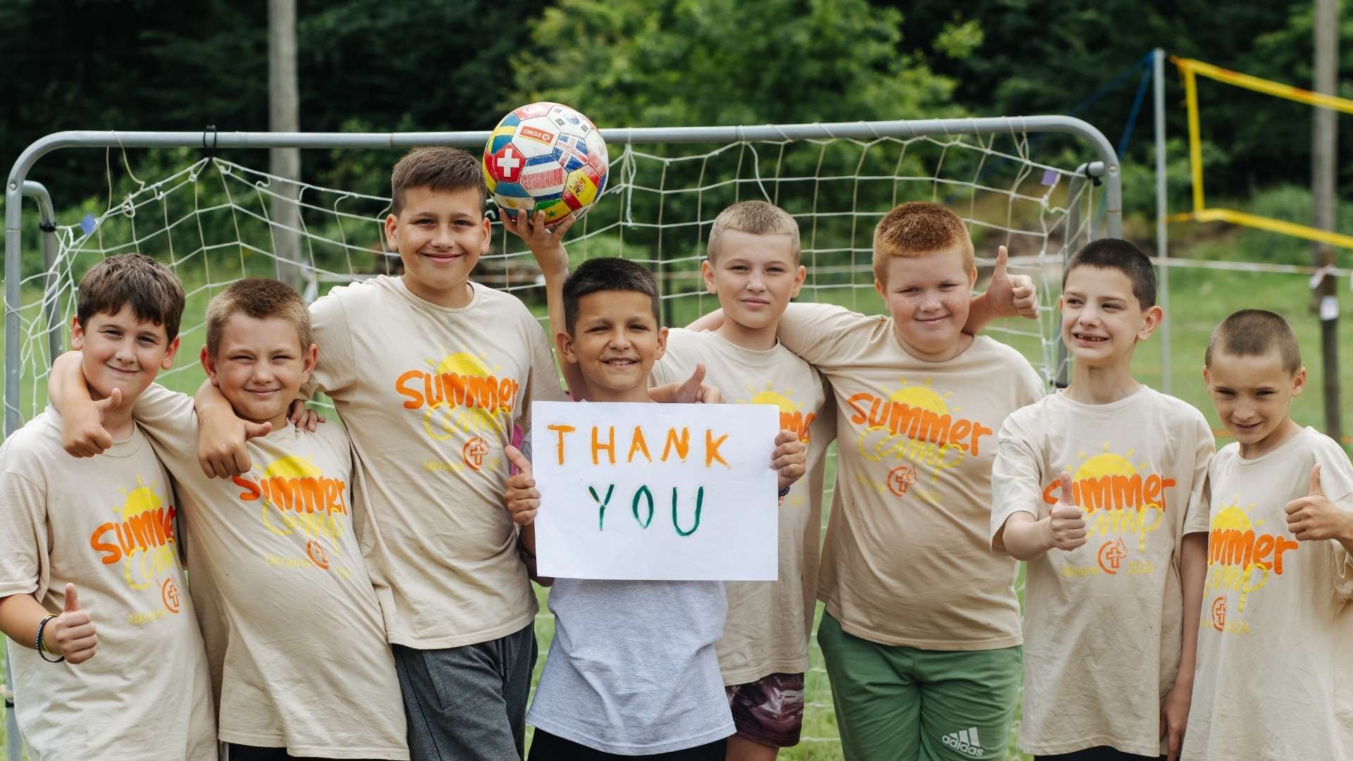 Group of young boys in matching t-shirts holding up a soccer ball and a thank-you sign.