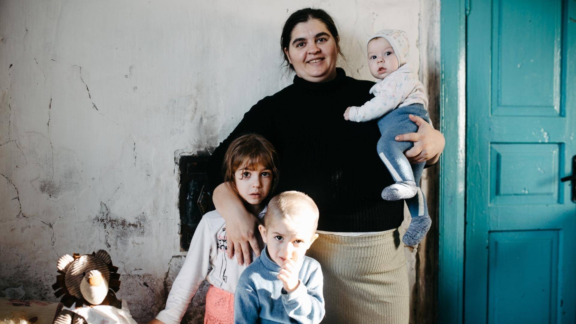 A mother with her three children in a sparsely furnished, dilapidated room.