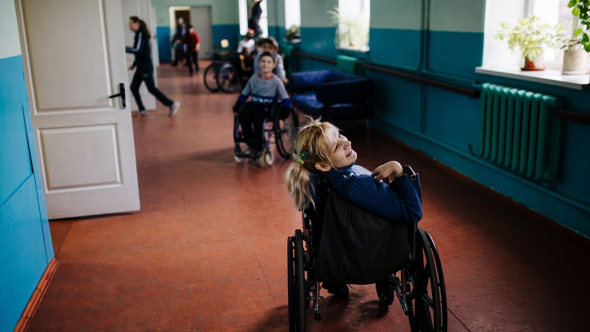 A group of young adults in wheelchairs in a bright hallway.