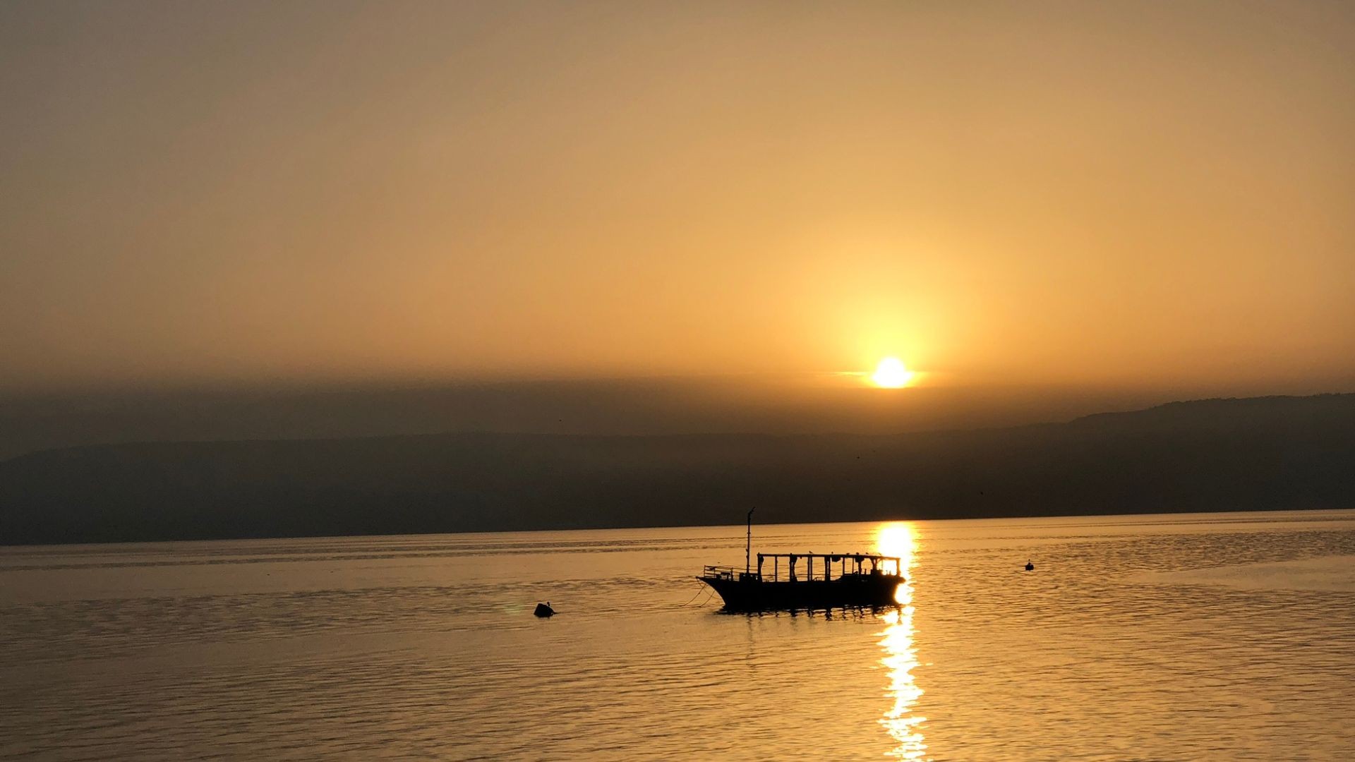 Small boat rests on the calm waters of the Sea of Galilee at sunset, sky glowing softly in a peaceful evening scene.