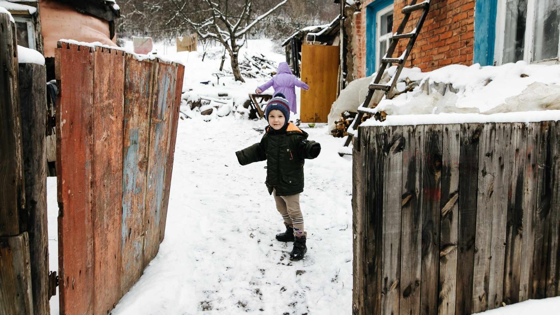Child turns back while running through gate into snowy yard by the house.