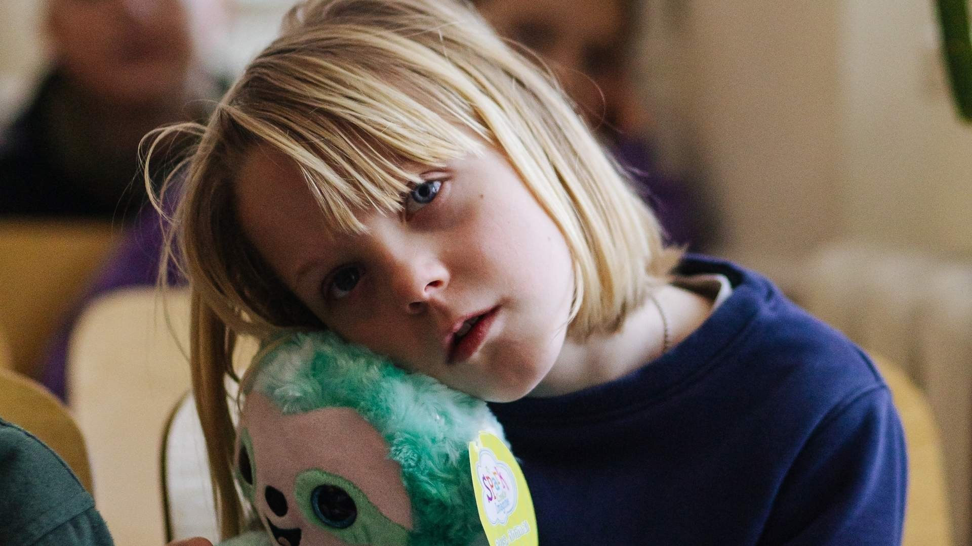 A young Ukrainian girl hugs a new soft toy, looking sad and seeking comfort.