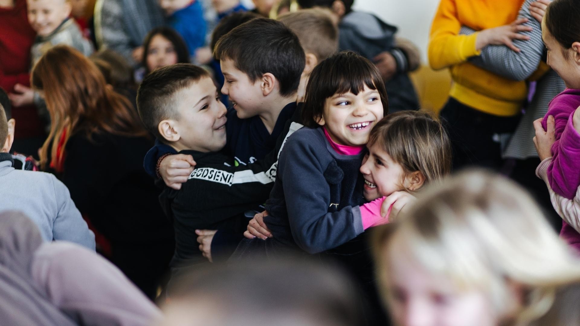 A classroom of children joyfully hug each other.