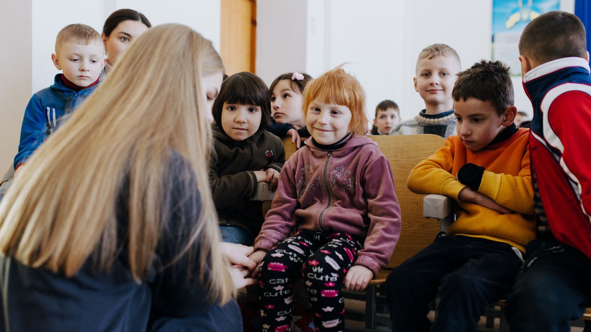 A young girl smiles as Eugeniya kneels, takes her hand, and speaks to her.