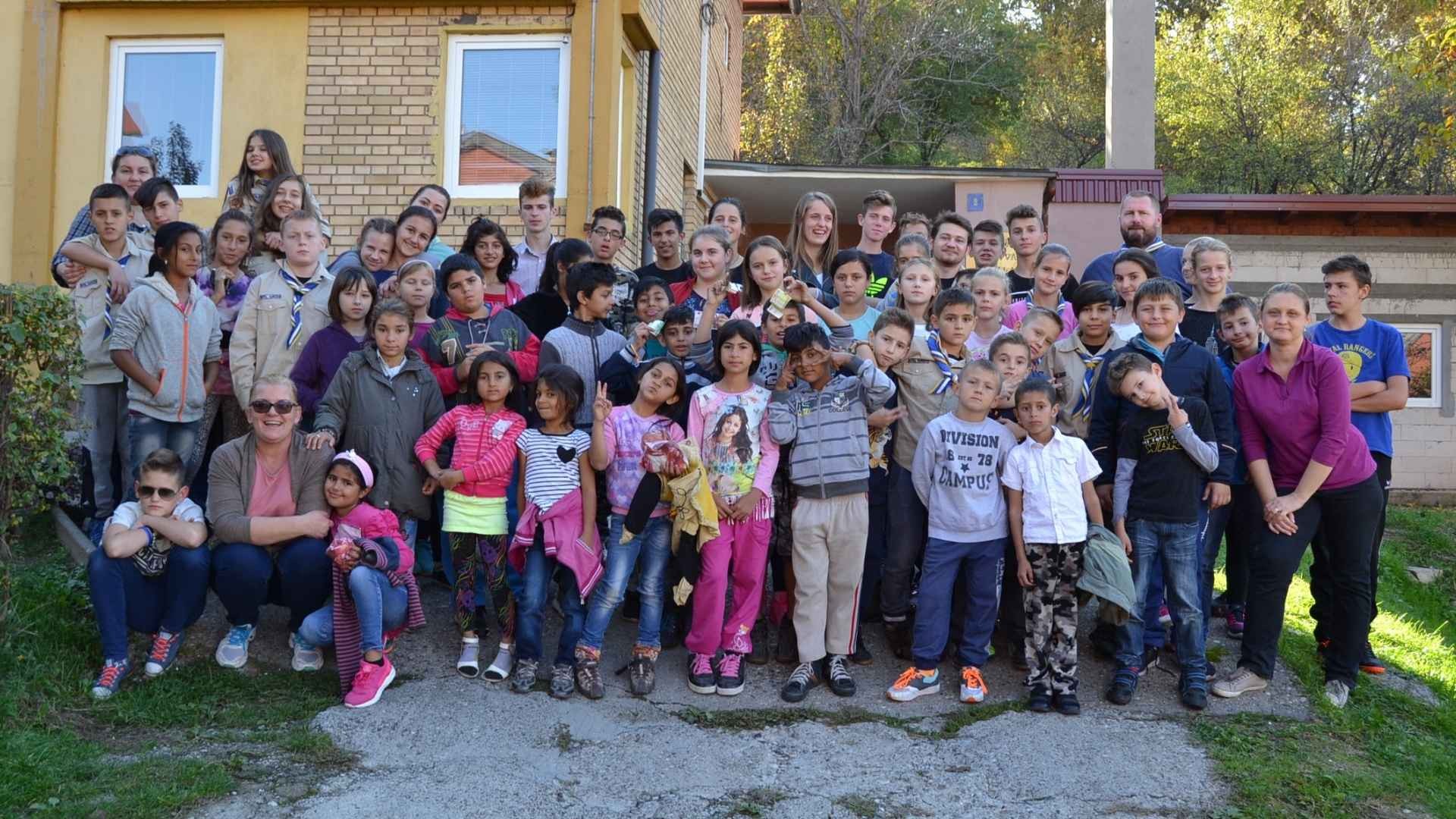 Children and young adults gather outside, smiling for a fun group photo.