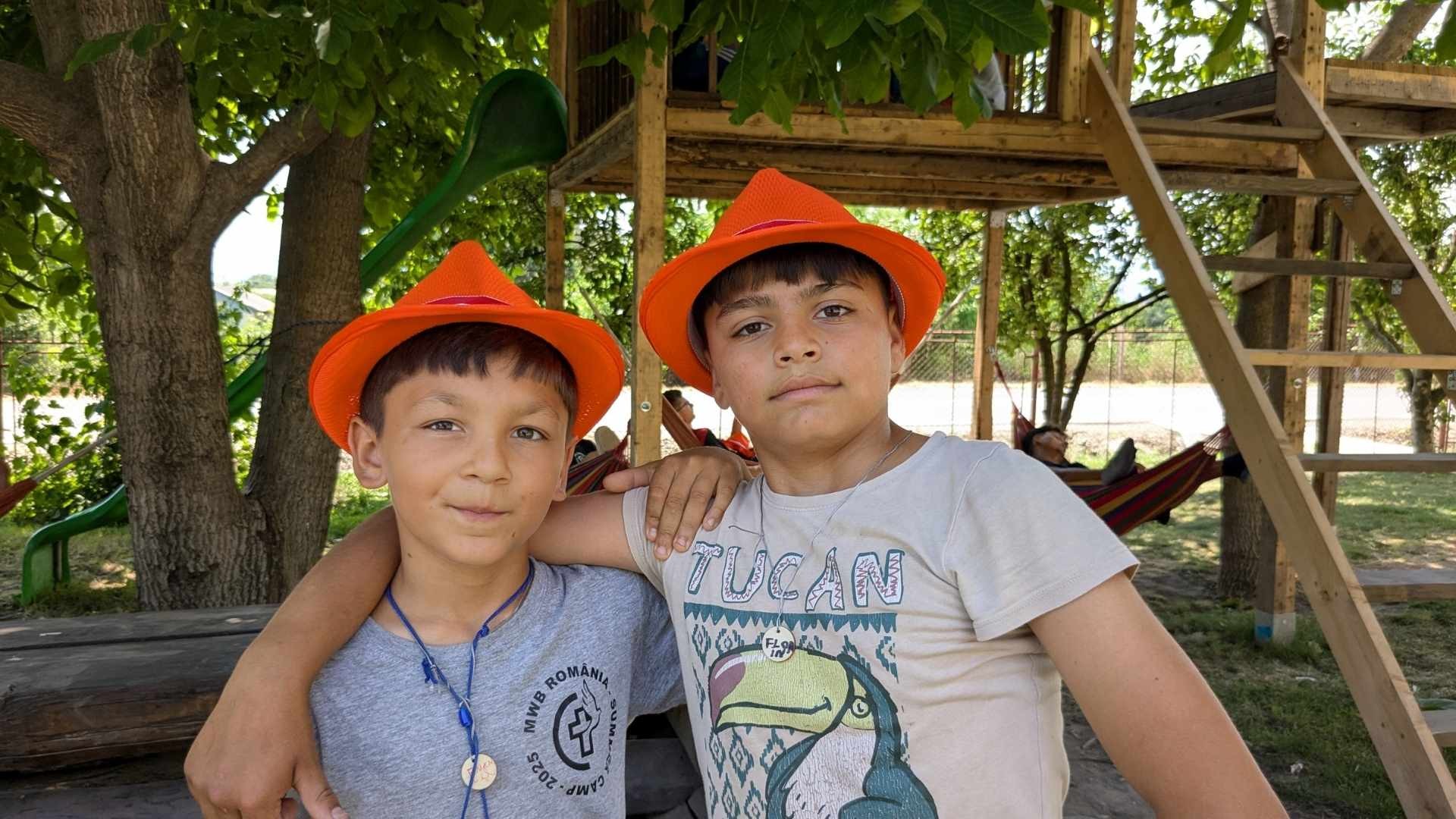 Two teen boys in orange hats stand with arms around each other.