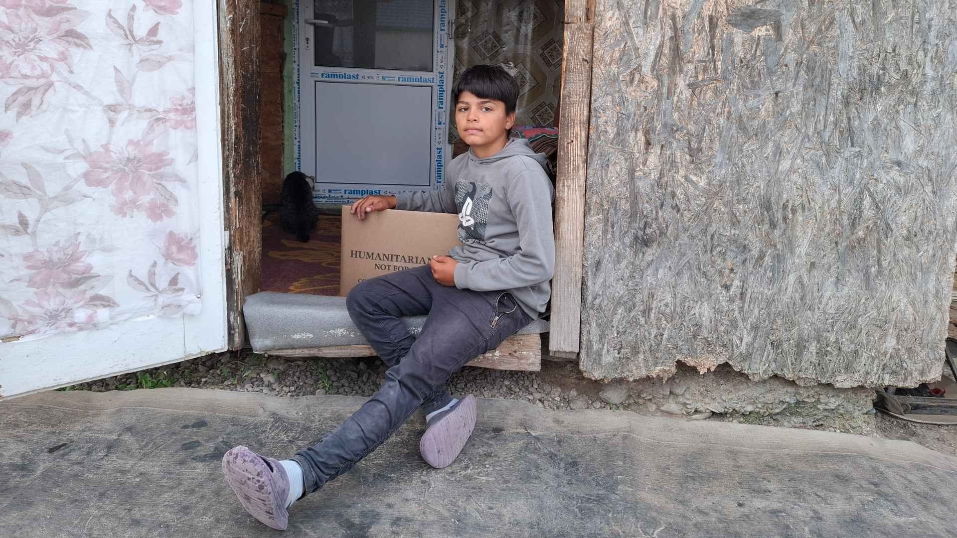 Teen boy sits quietly in the doorway of his worn home.