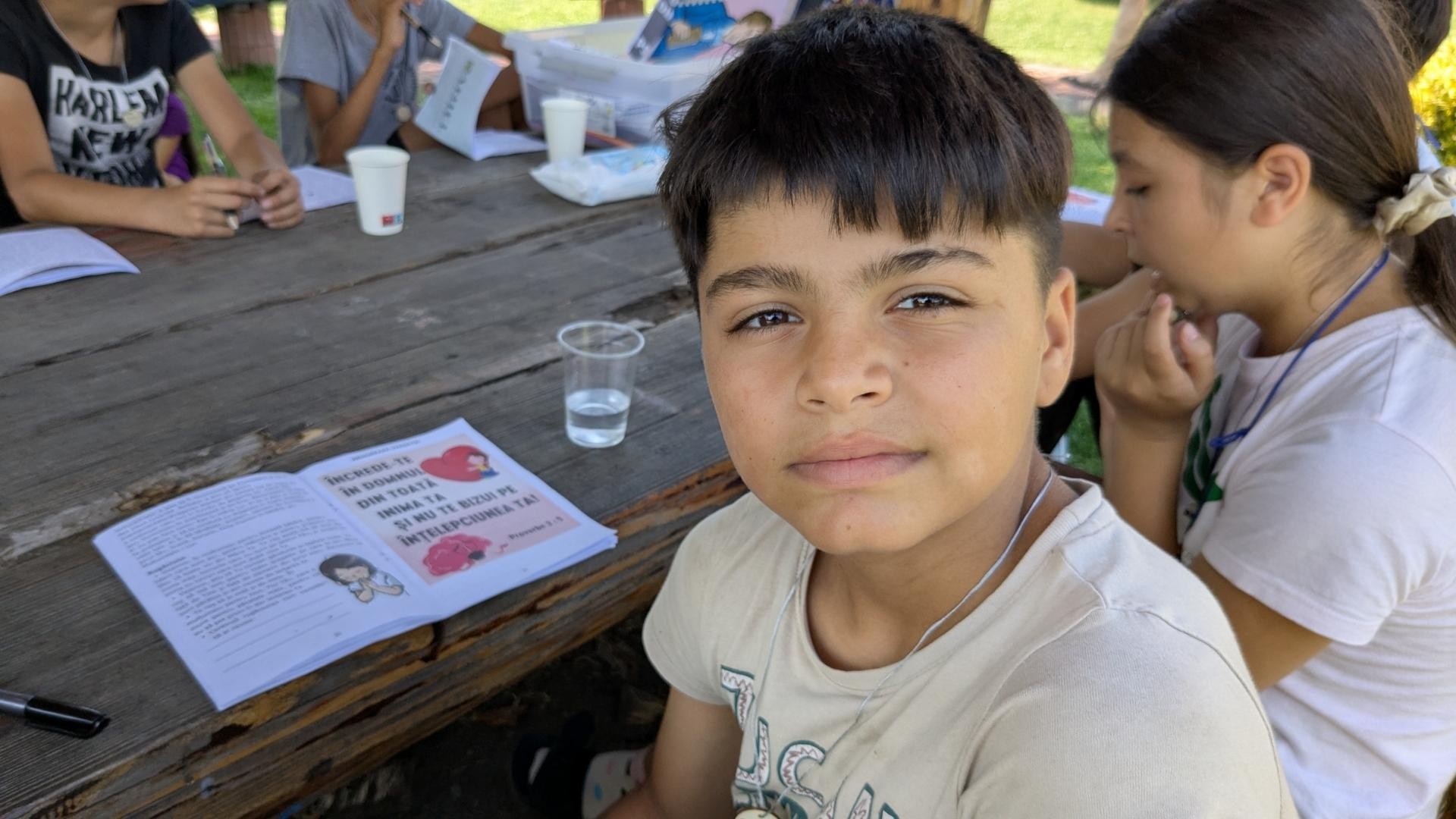 Teen boy glances back with Bible study book and others gathered at deck table.