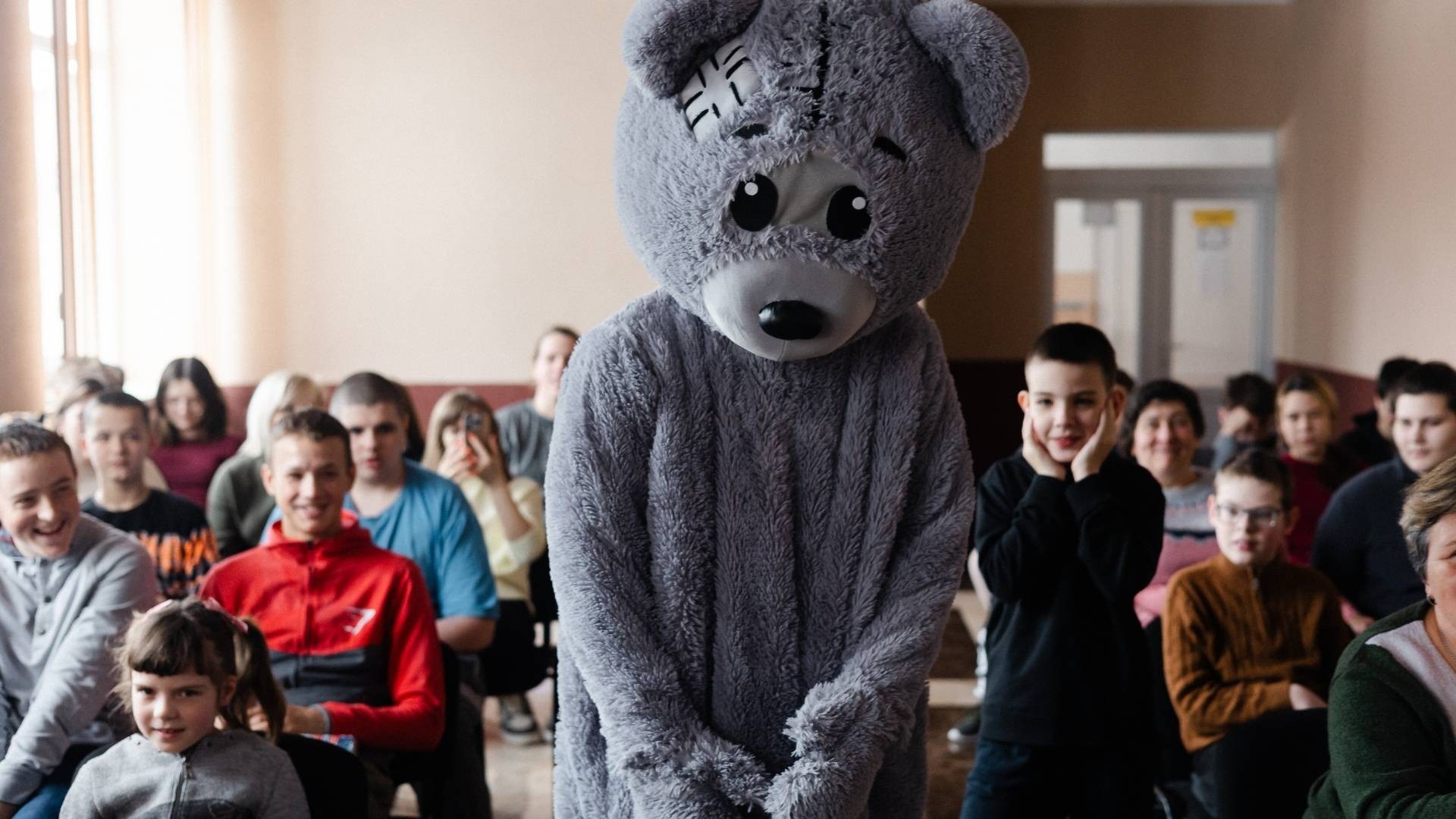 Upanchik, the large grey bear, walks through a room of laughing children.