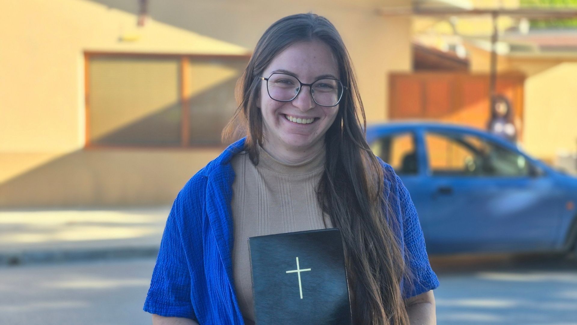 Anelia holds her Bible close, smiling joyfully, radiating warmth and faith in a heartfelt moment.