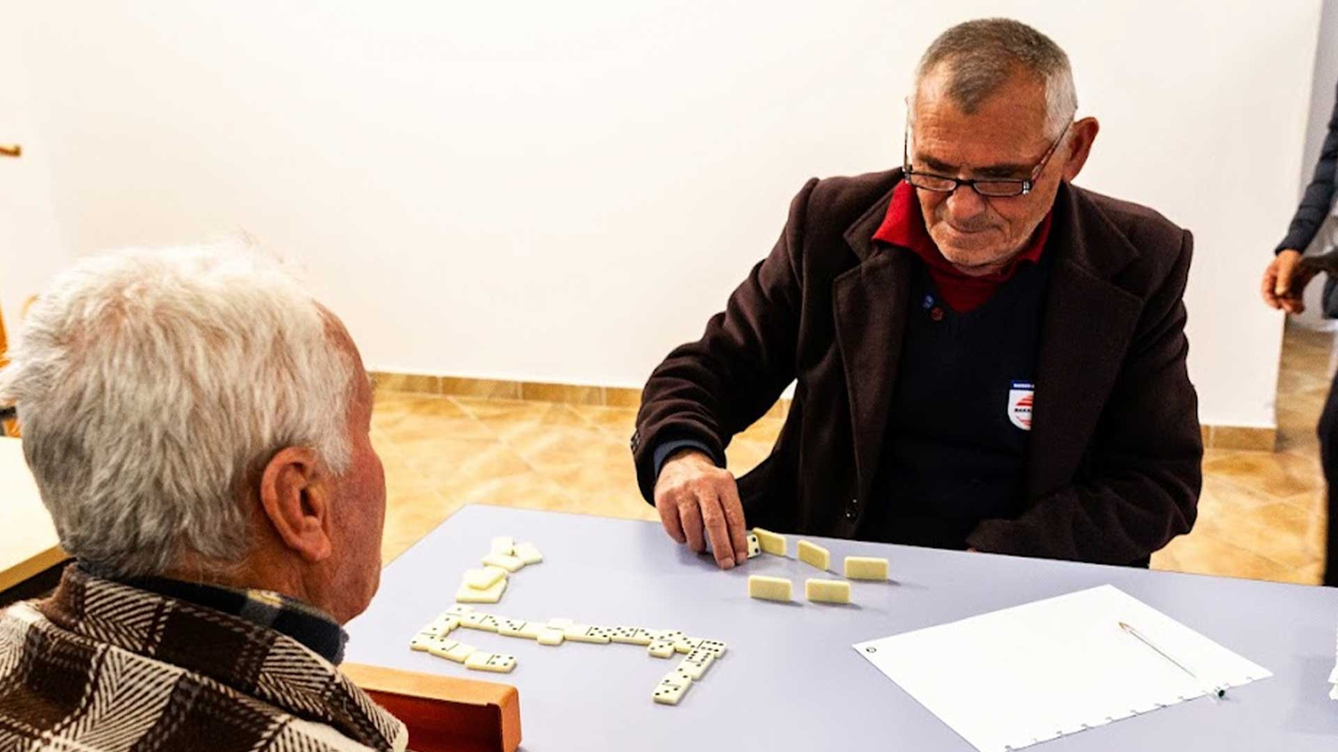Misir, an elderly man, smiles as he plays dominos with a church friend.