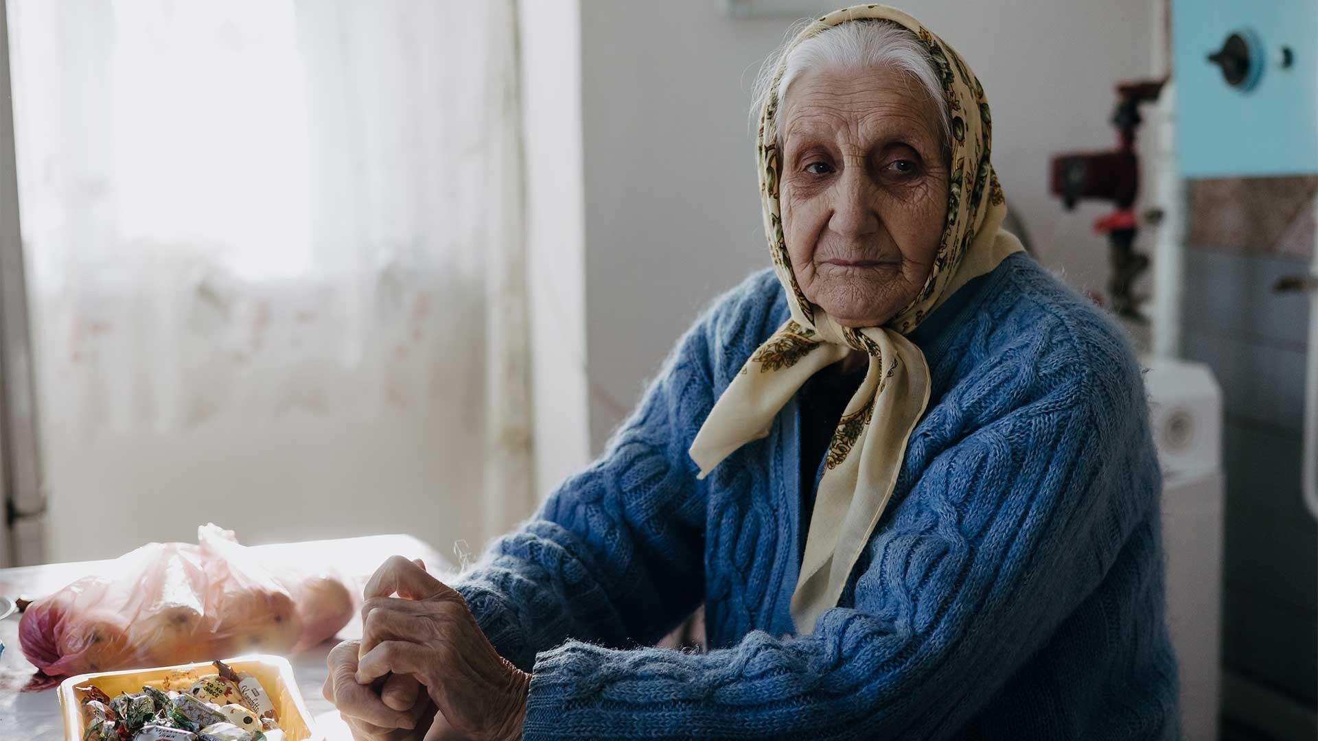 Elderly widow Galyna sits at the kitchen table, weary and deep in thought