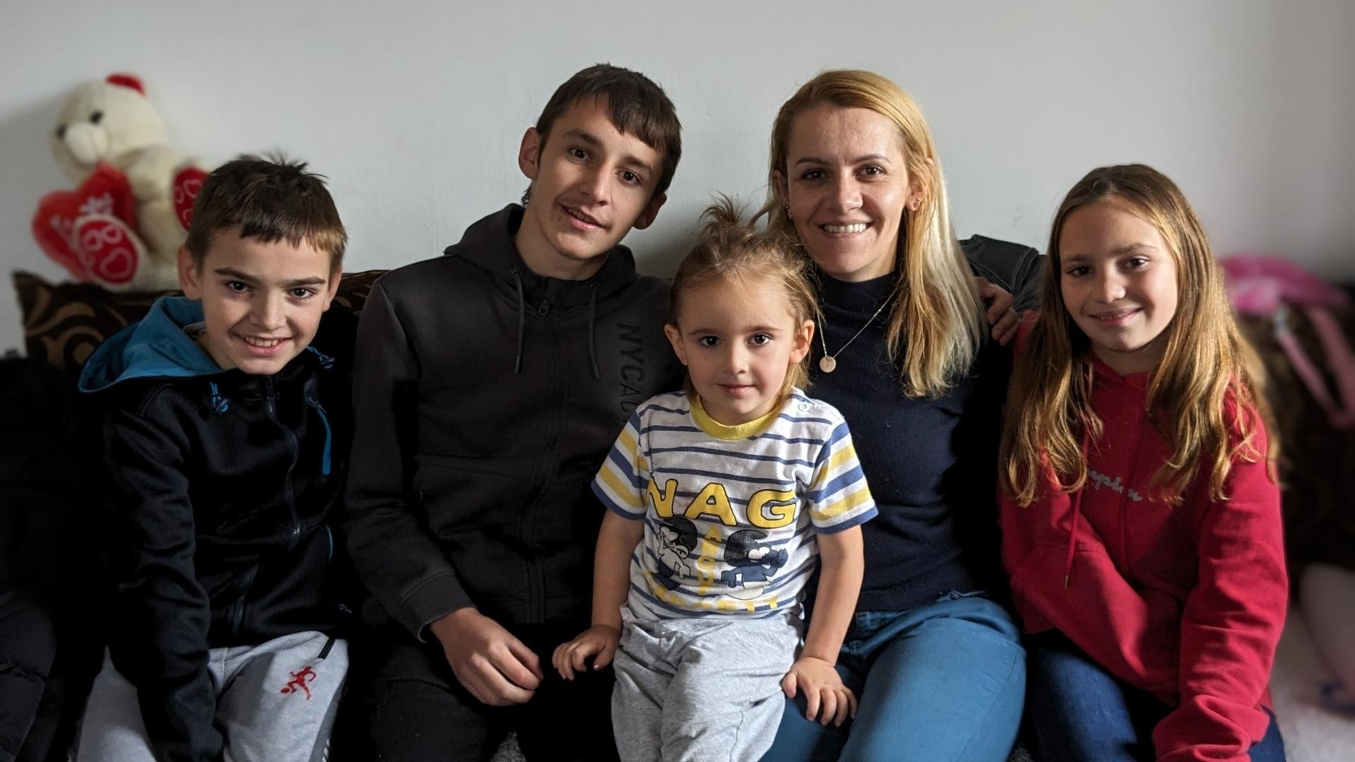Smiling mother with four children sit together on a couch in their home.
