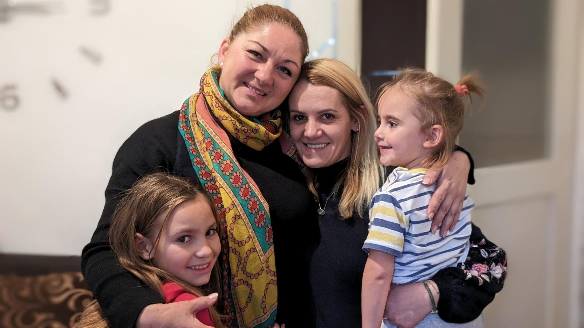 Two women and two children stand close, arms around each other, smiling.
