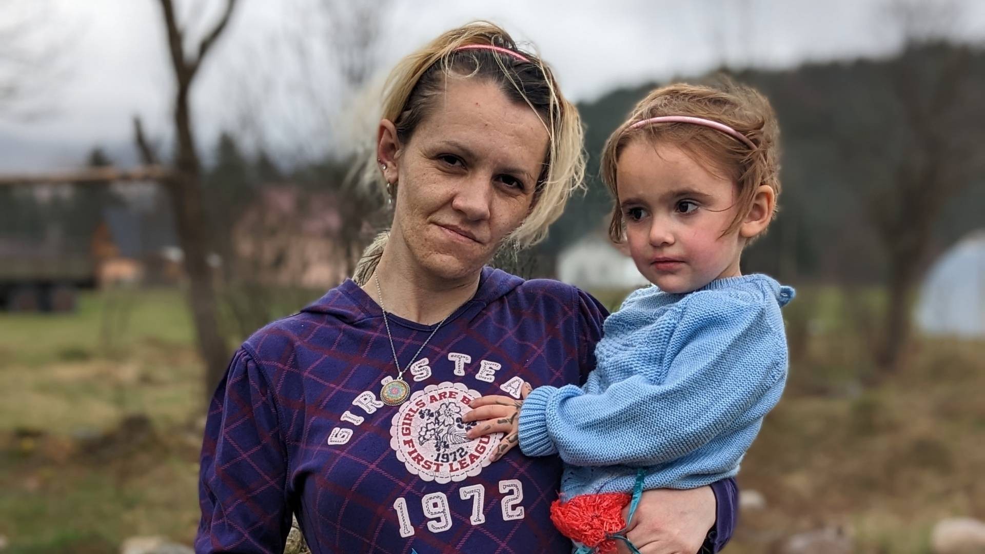 Young mother holds child on her hip, her tired face hints at hardship.