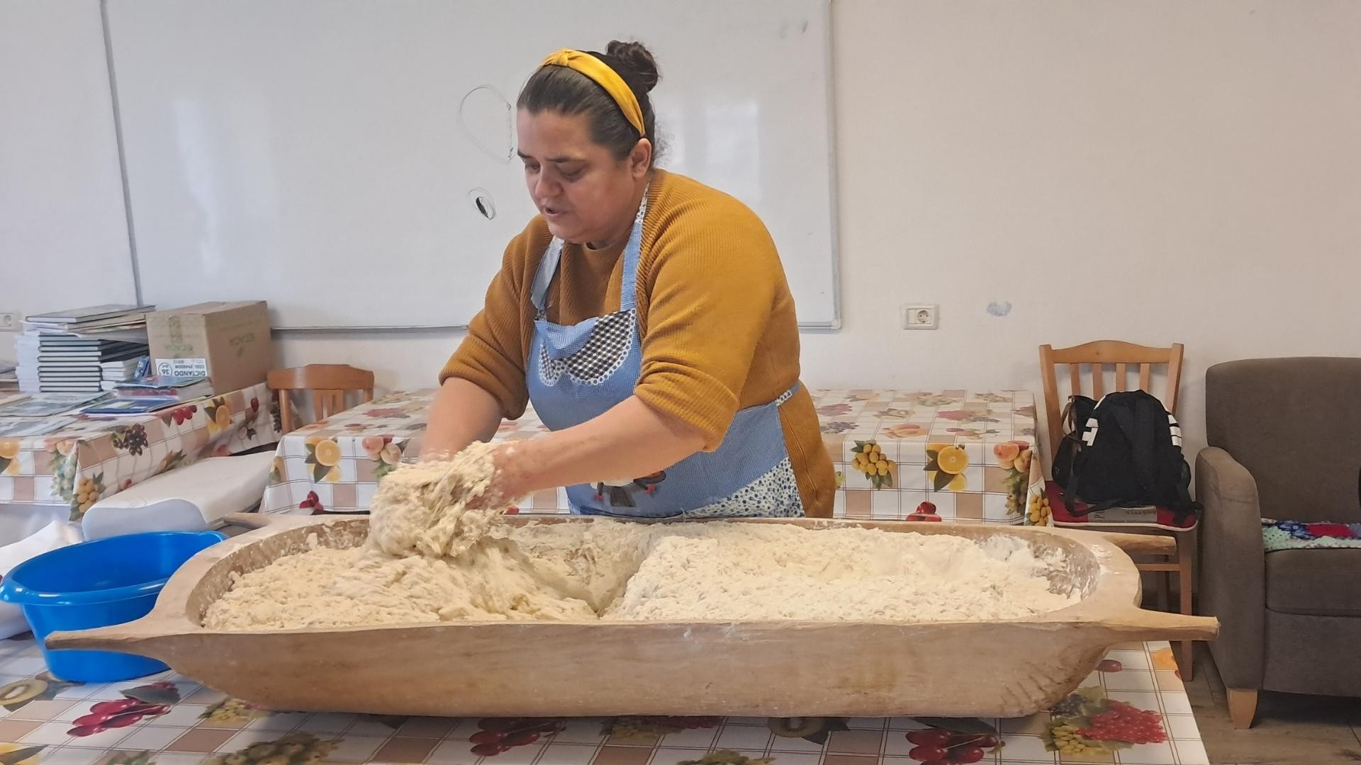 Maria kneads dough in a large wooden trough