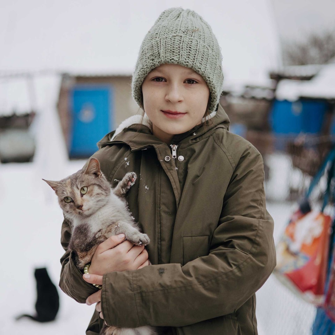 Young Sofiya stands in a snow-covered yard, holding her cat.