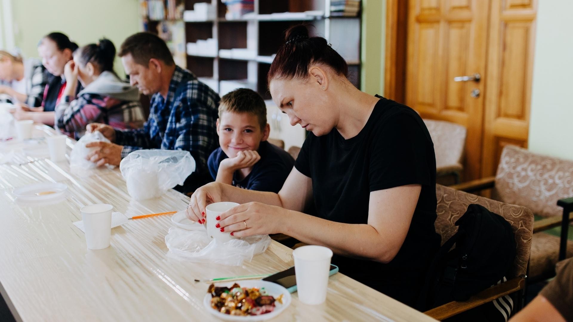 Ukrainian refugees sit together at a table, repairing broken cups during art therapy.