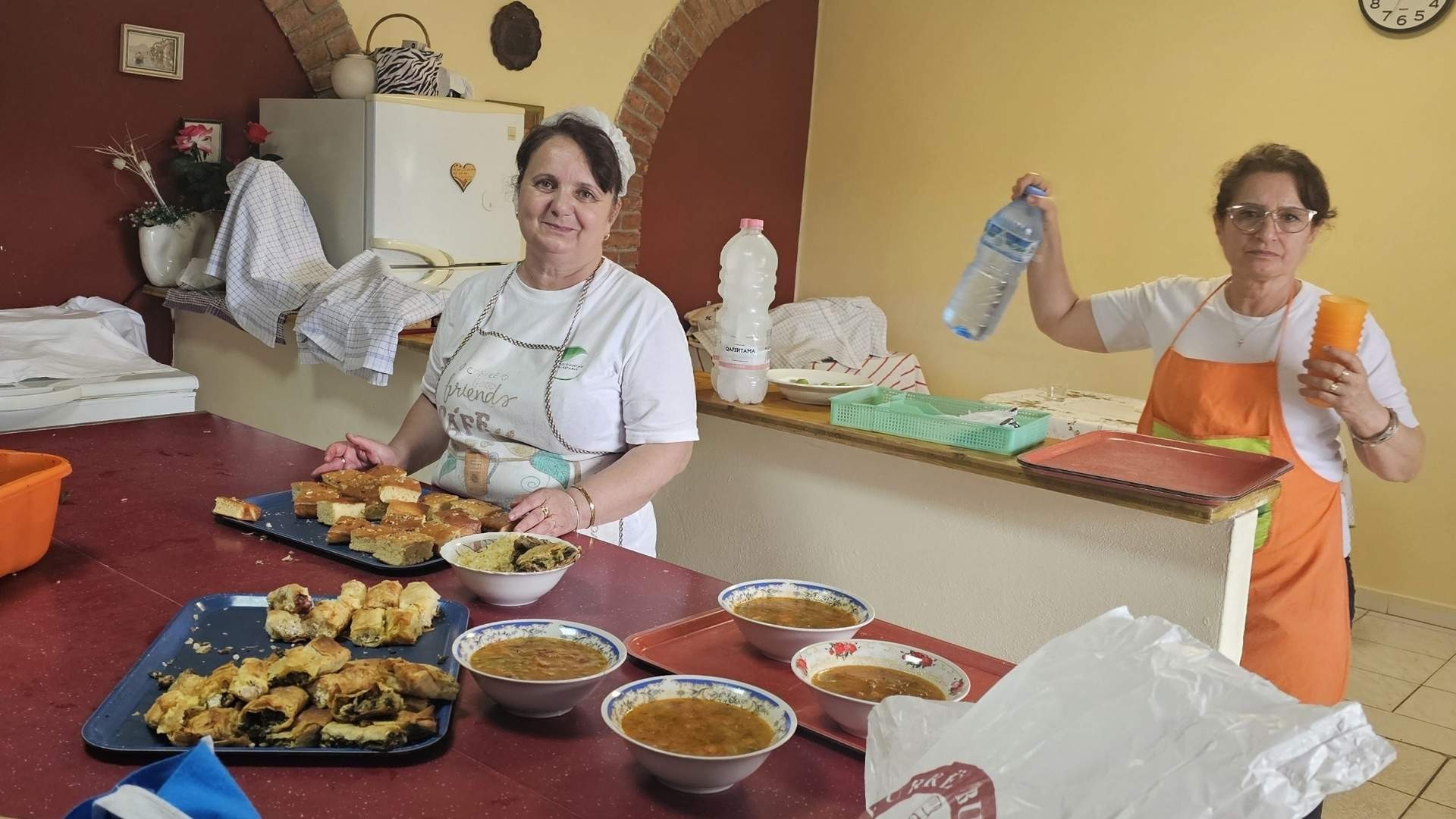 Two soup kitchen staff prepare food together, readying meals for guests.