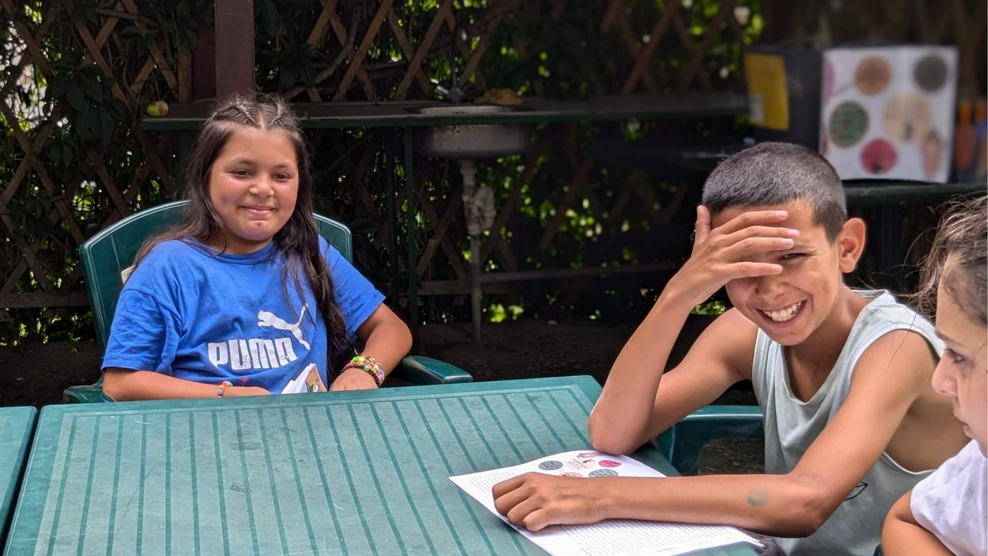 Group of children laughing together while sitting outdoors around a table.