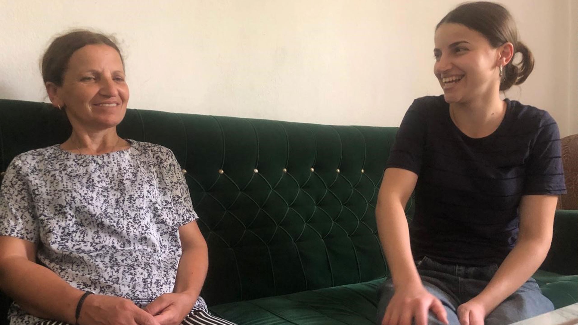 Two women sitting on a green sofa, sharing a joyful moment together.