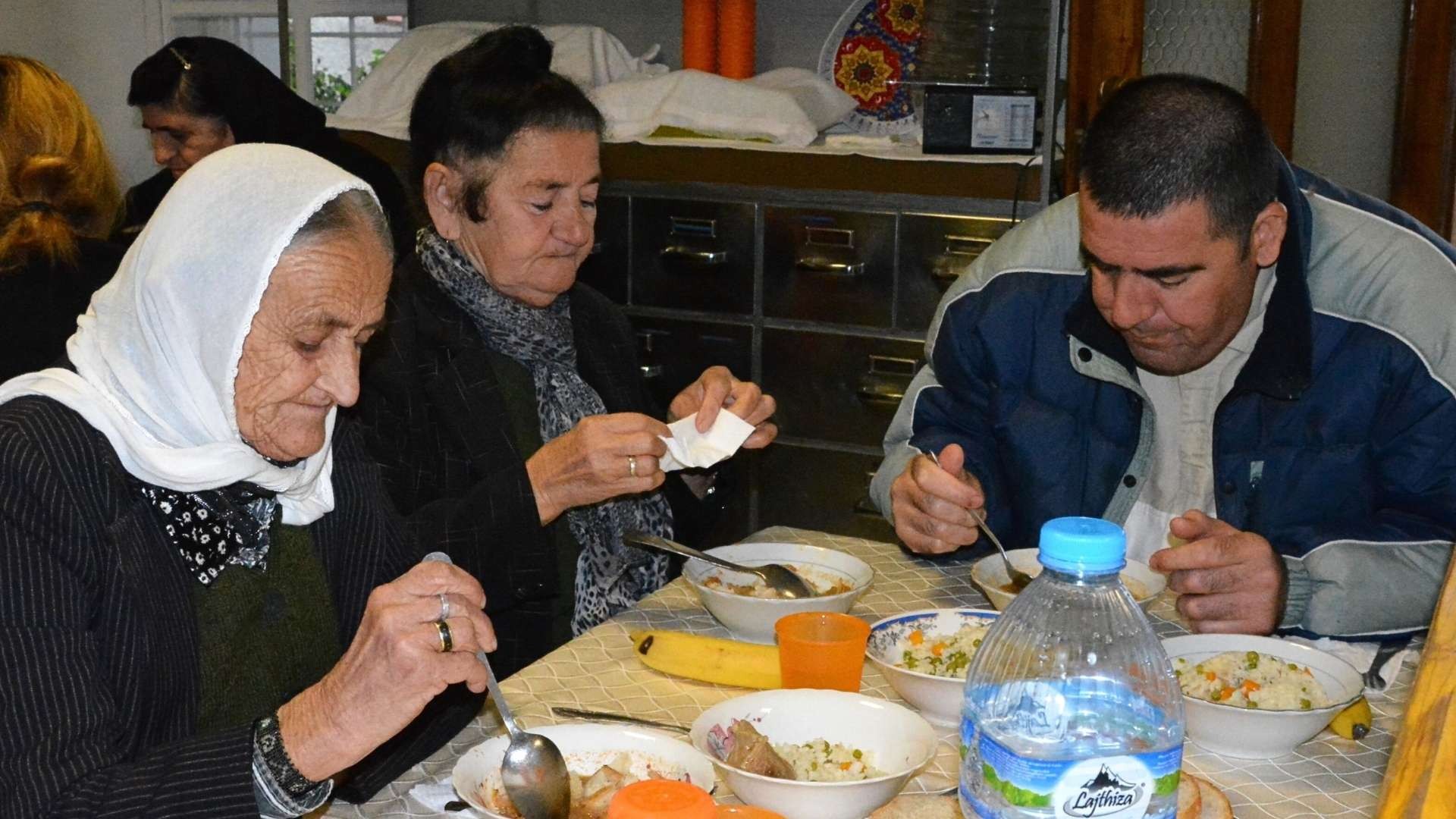 Two elderly women and a man sitting at a table, enjoying a warm meal together.