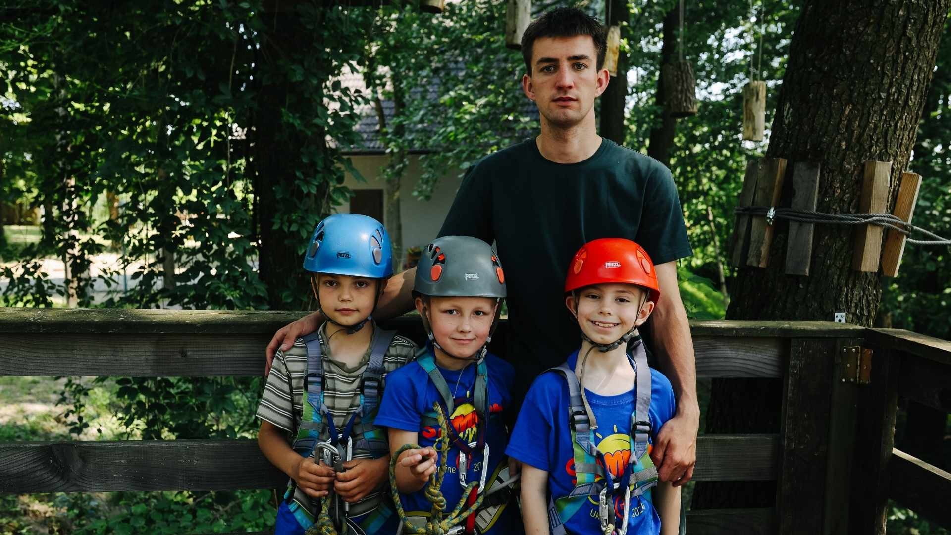 Young boys geared up for ziplining, standing with a supportive adult camp leader.