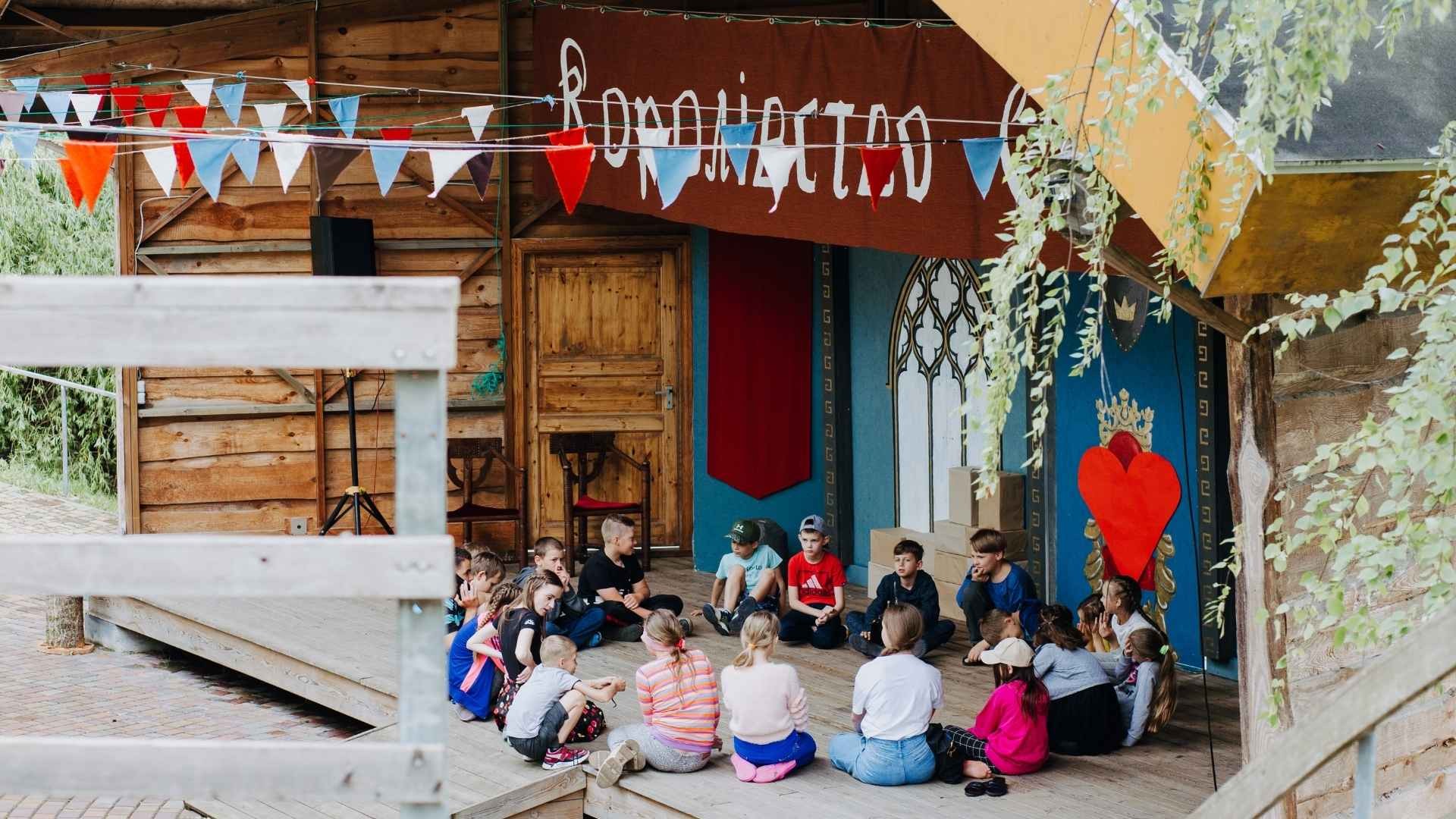 Young campers seated closely in a circle on a wooden deck, sharing in a group discussion.